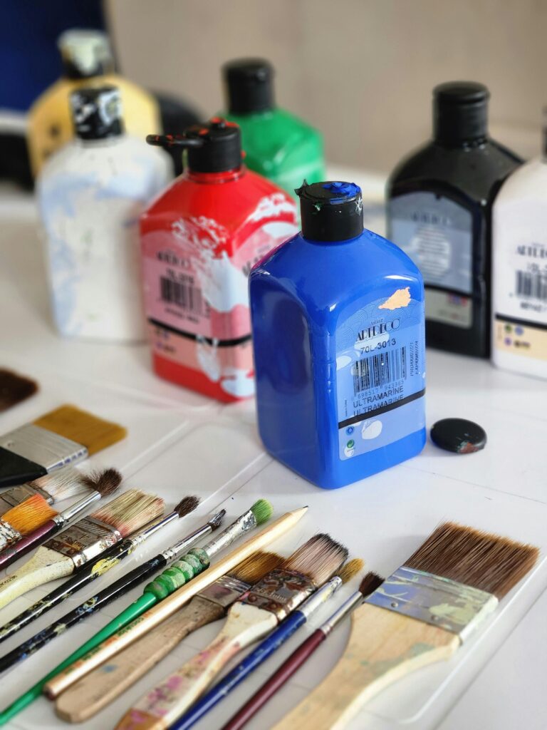 Acrylic paint bottles on a desk with paint brushes.