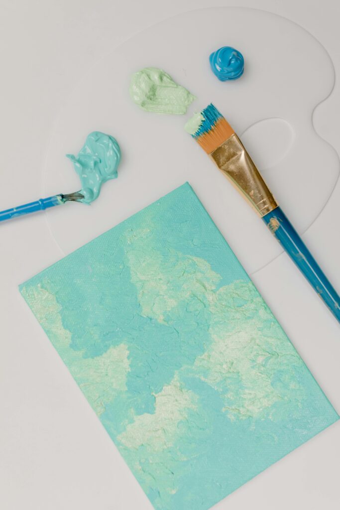 Acylic painted canvas in front of a painters palette with two acrylic brushes.