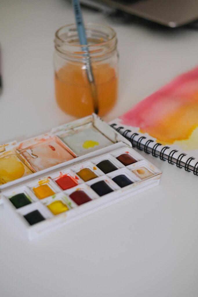 Watercolor pan paints next to water jar and sketch book.